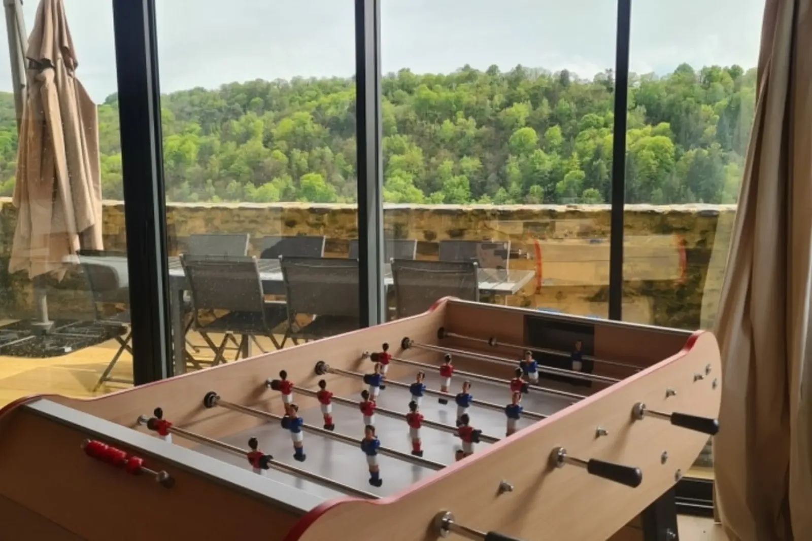 Table football in front of the living room's picture windows, opening onto the terrace and the wooded hillside
