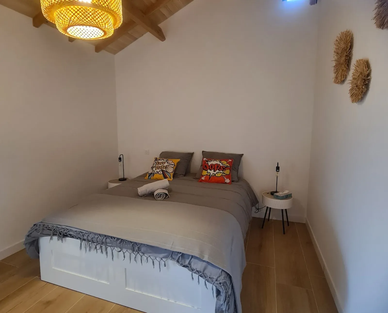 Bedroom under a wooden ceiling with a double bed, bamboo pendant light and raffia wall decorations