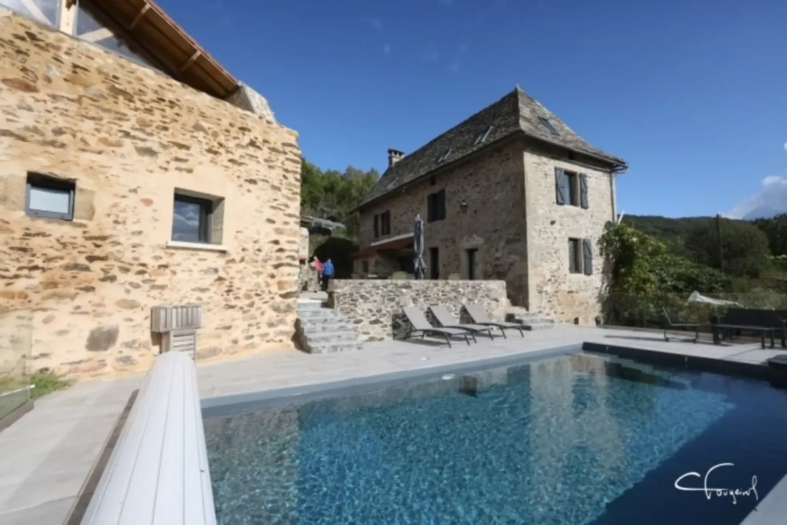 The two stone houses of Aubié, with sun loungers and the pool in the foreground, in Latouille-Lentillac