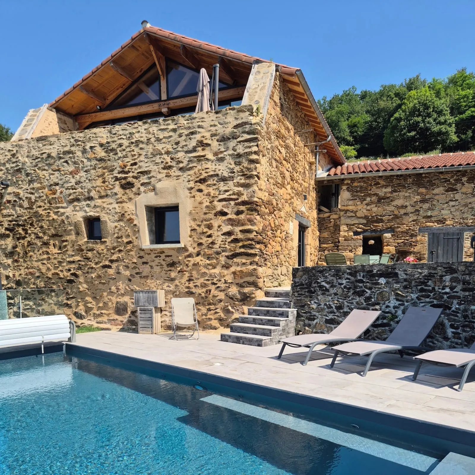 Restored stone barn with its large glazed gable, above the pool lined with sun loungers