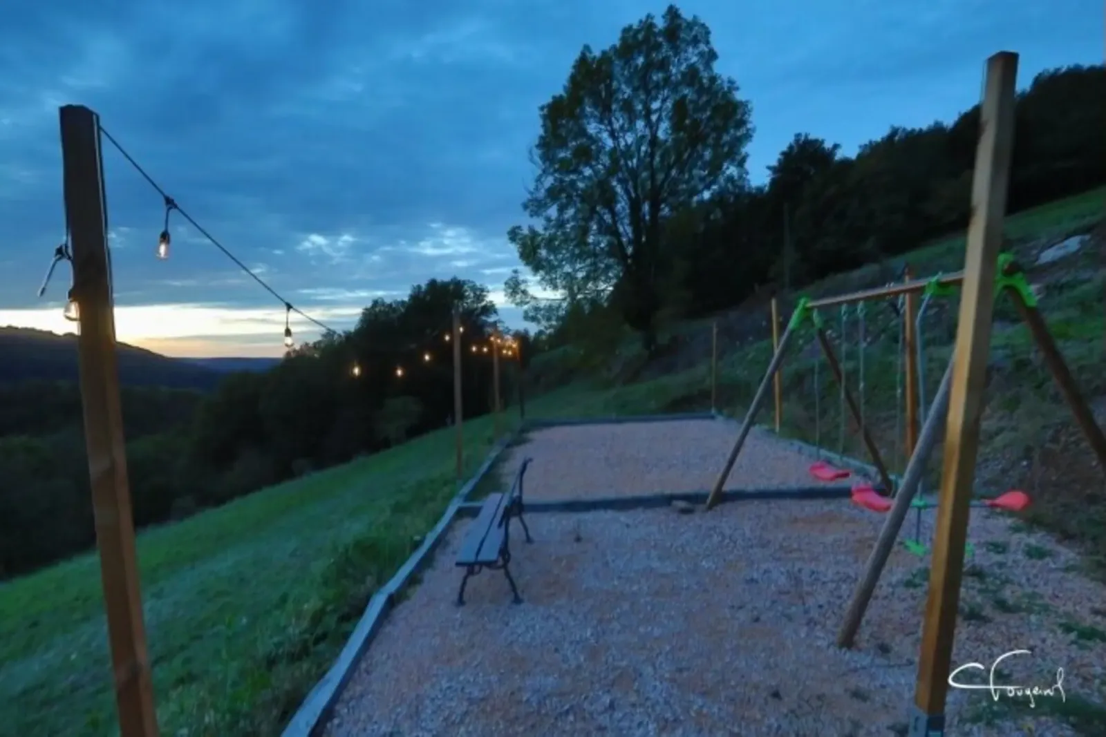 Pétanque court, bench and swings under string lights at dusk, facing the valley