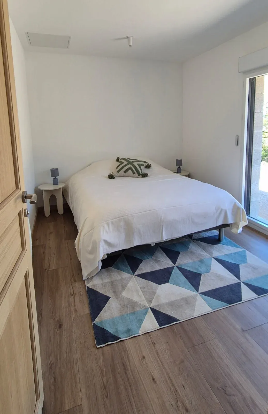 Chambre avec lit double, tapis géométrique bleu et porte-fenêtre