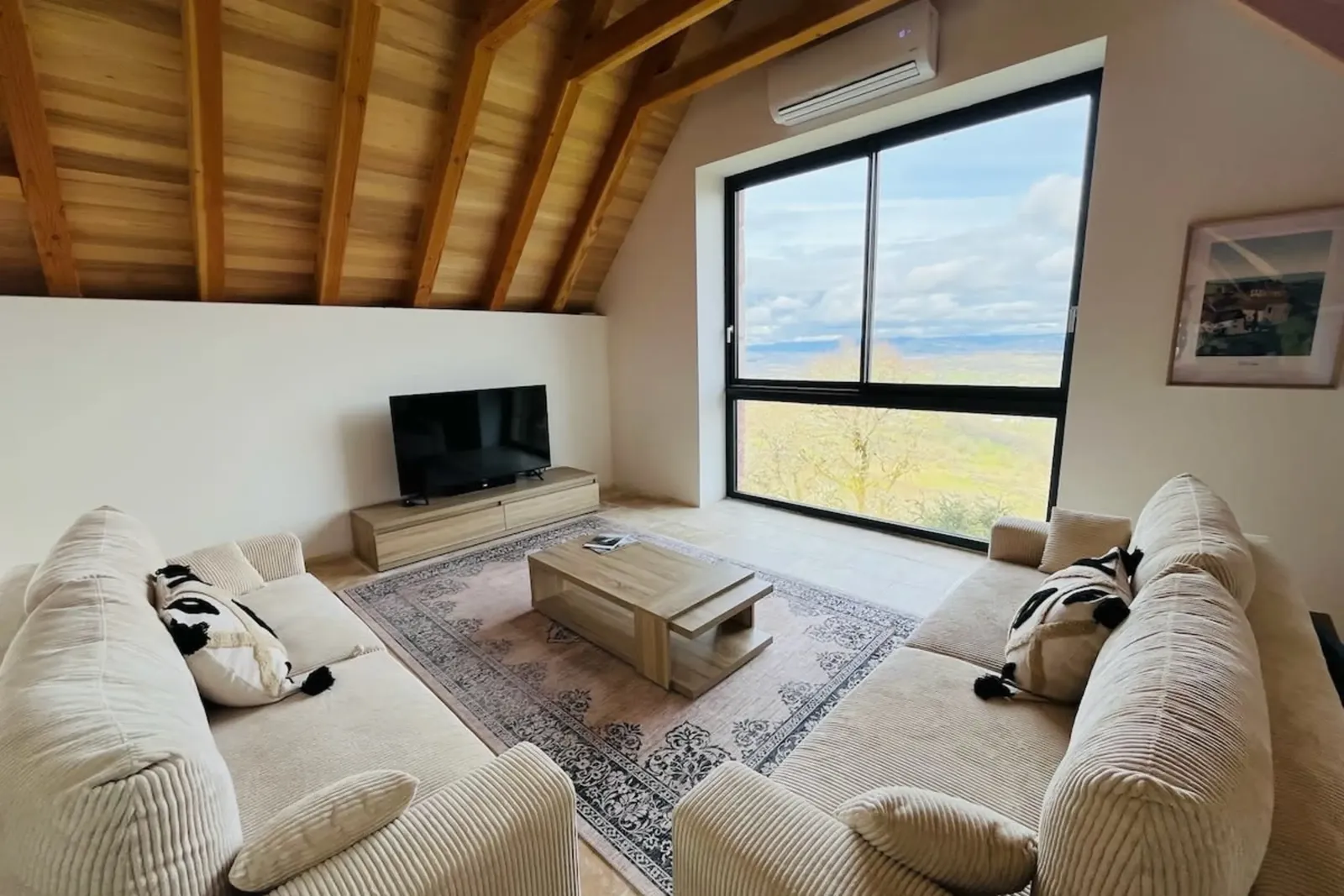 Salon avec deux canapés, table basse et téléviseur, face à une grande baie vitrée