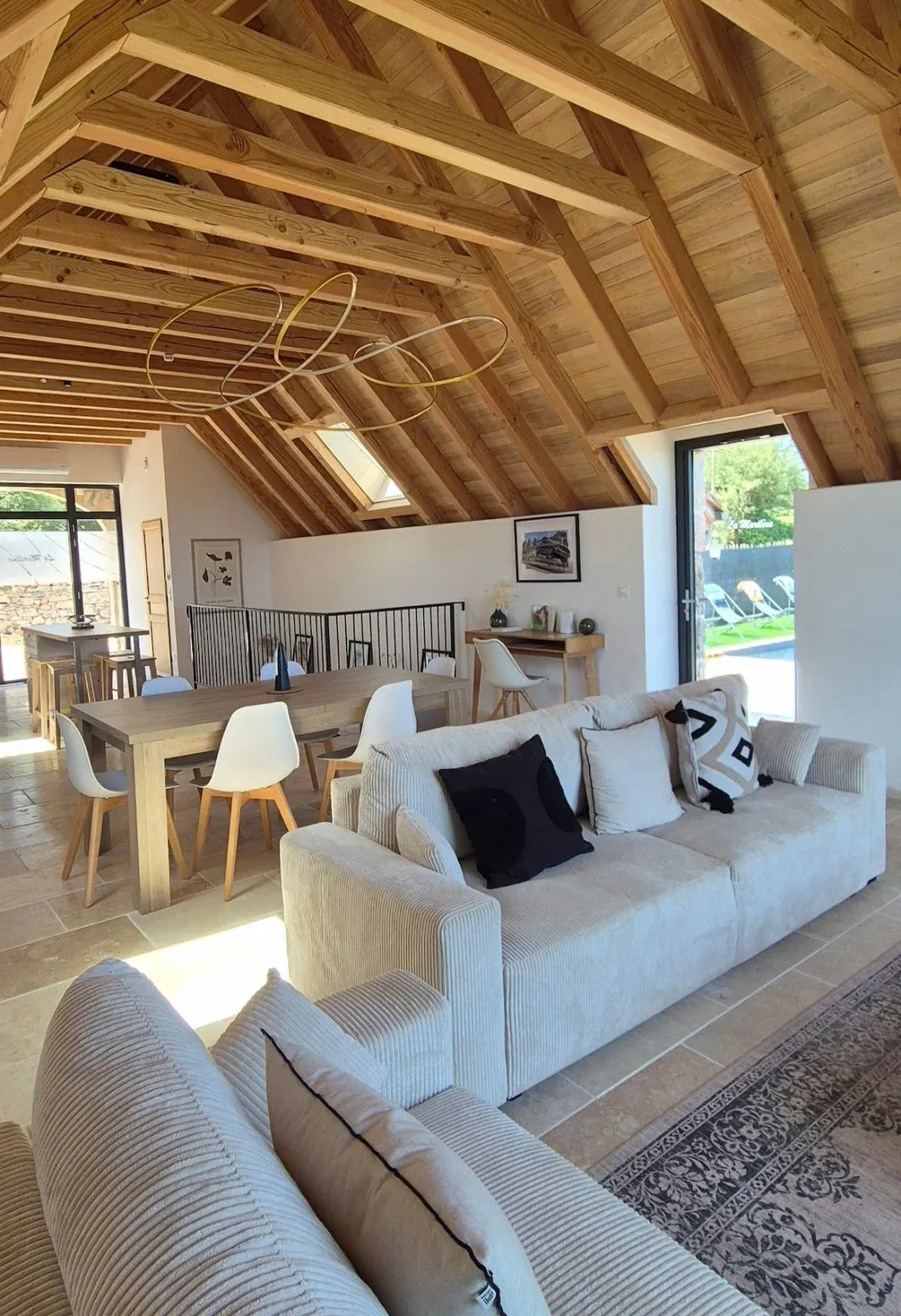 Pièce de vie sous charpente apparente, avec canapés, grande table et accès à la piscine