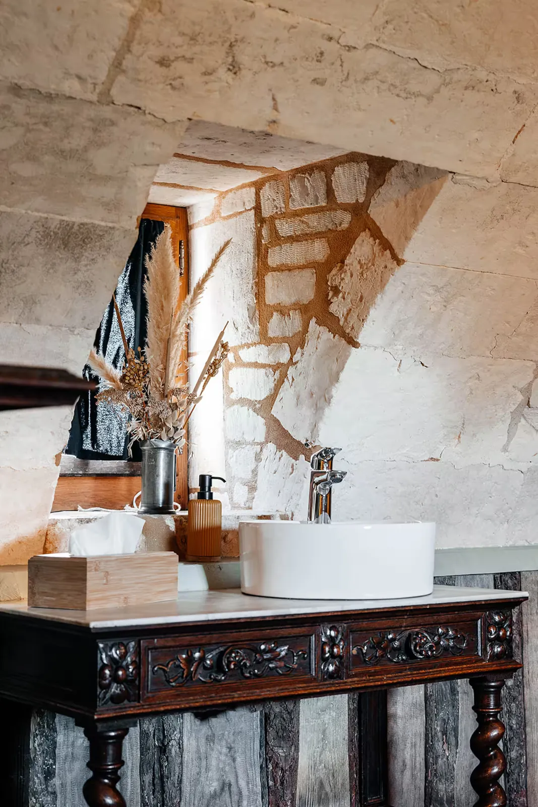 Vasque sur meuble ancien sous un mur de pierre voûté, salle de bains de La Motte Féodale