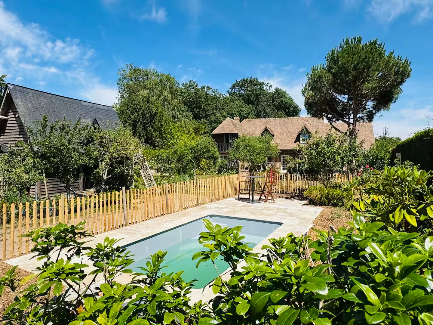 Piscine extérieure chauffée entourée de végétation et de ganivelles, dans le jardin du Clos du Veneur au Mesnil-Jourdain