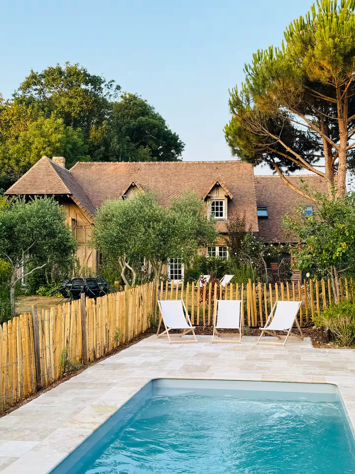 Piscine et sa terrasse en pierre naturelle avec transats, devant la maison à colombages, Le Clos du Veneur