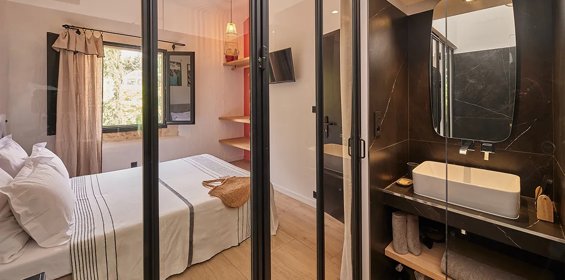 Chambre avec lit double et salle d'eau attenante derrière une verrière, Le Pin