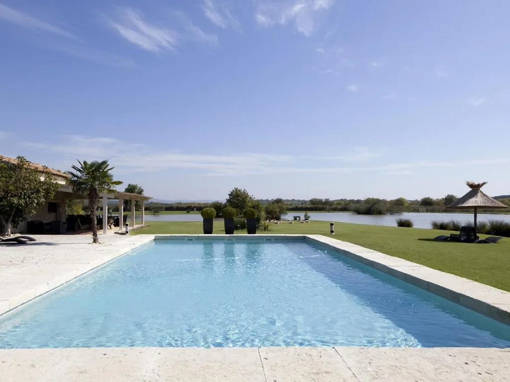 Piscine du Mas de la Galégière, bordée de pelouse et de parasols en paille