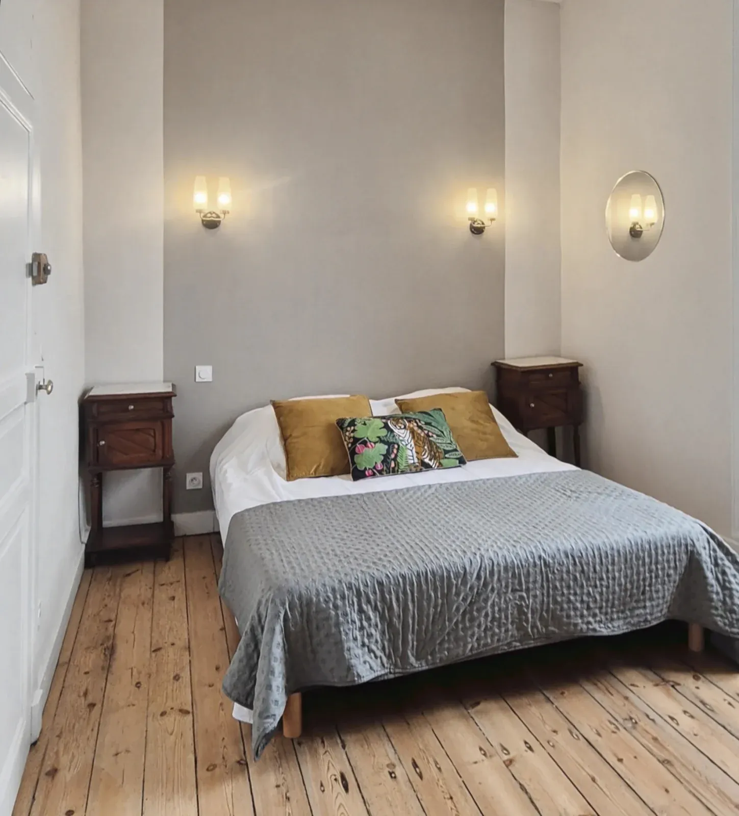Chambre avec lit double au jeté gris, coussins moutarde et coussin à motif tropical