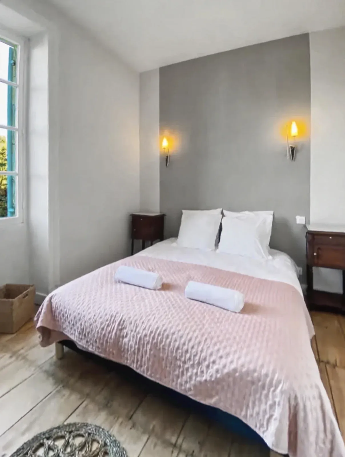 Chambre avec grand lit au jeté rose, appliques murales et tables de chevet anciennes
