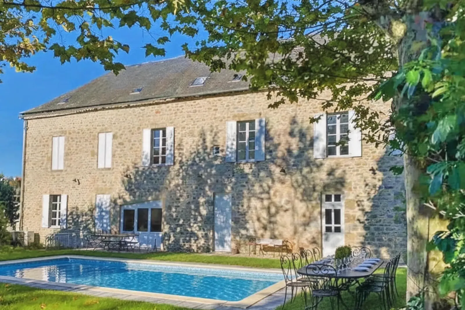 Façade en pierre de l'ancien hôtel, avec la piscine et la table de jardin au premier plan