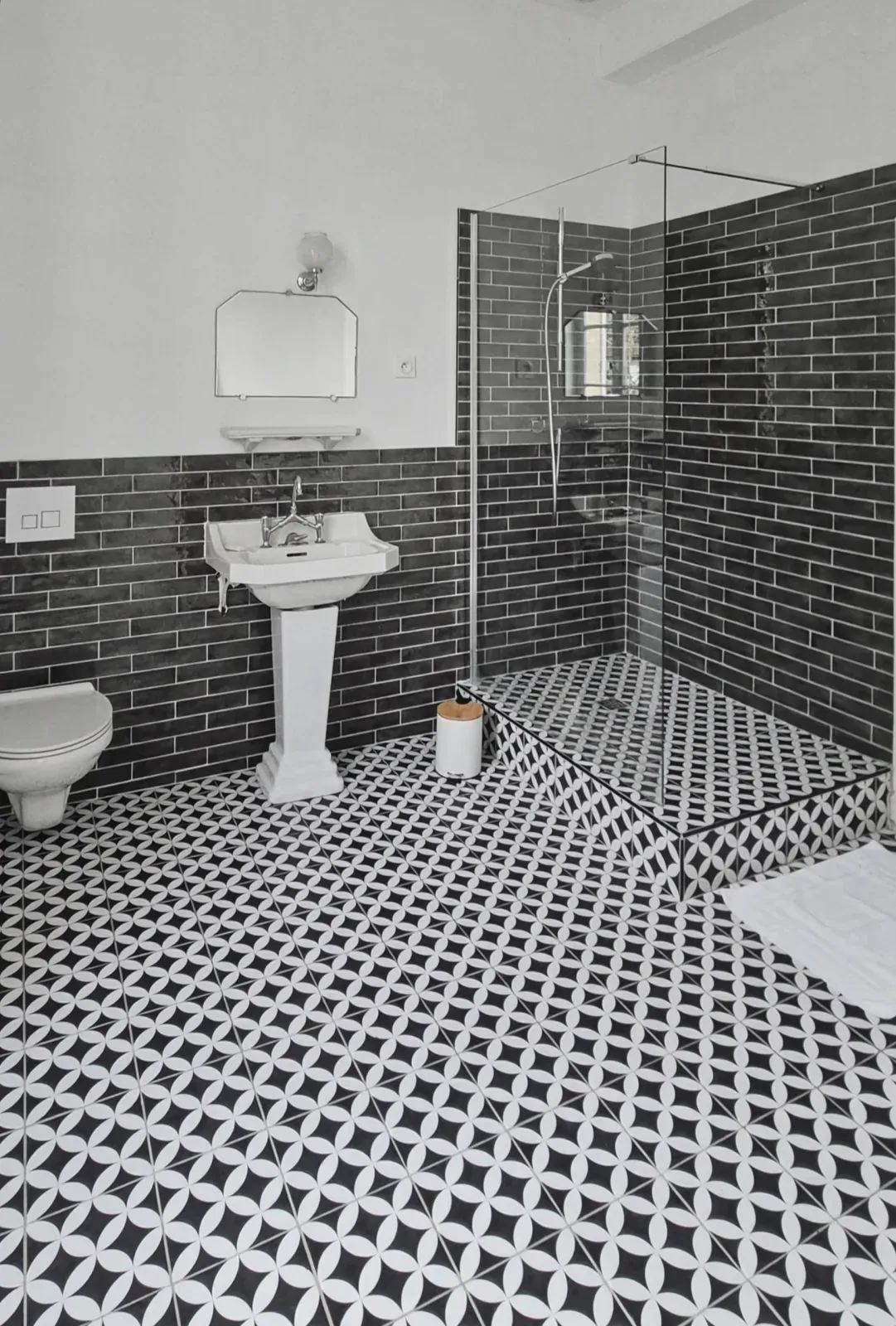 Salle de bains aux carreaux de ciment noirs et blancs, lavabo sur colonne et douche à l'italienne