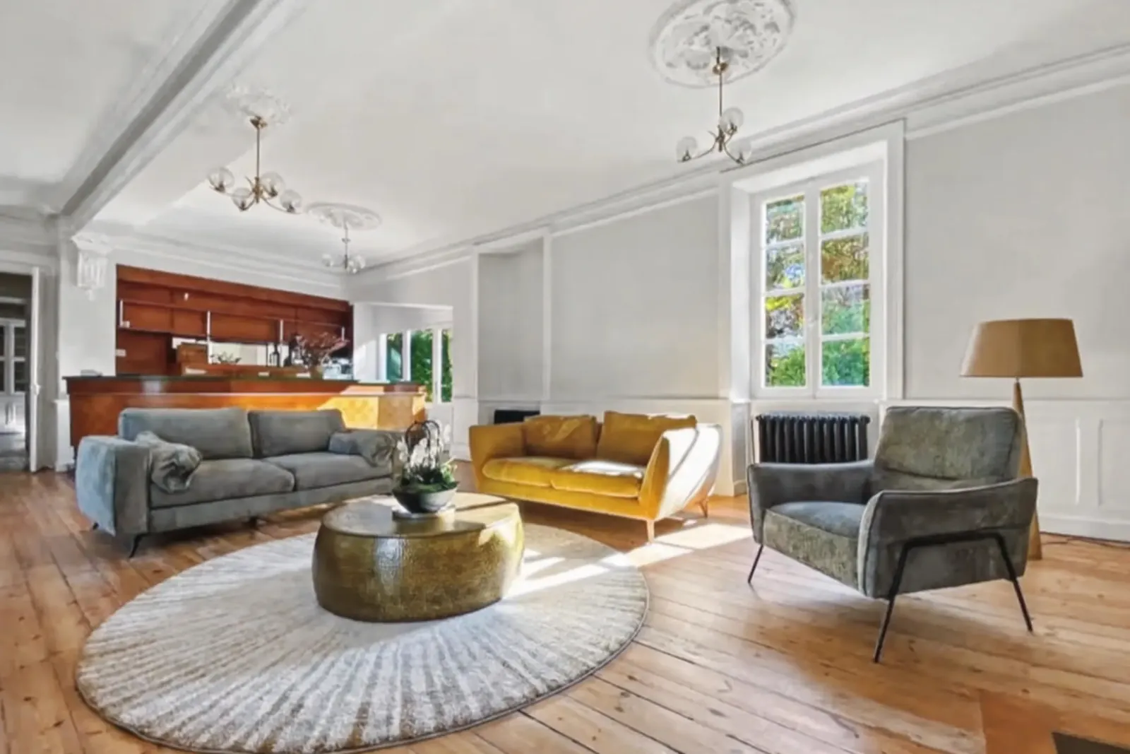 Grand salon aux parquets anciens, canapés autour d'un tapis rond et ancien bar-comptoir au fond