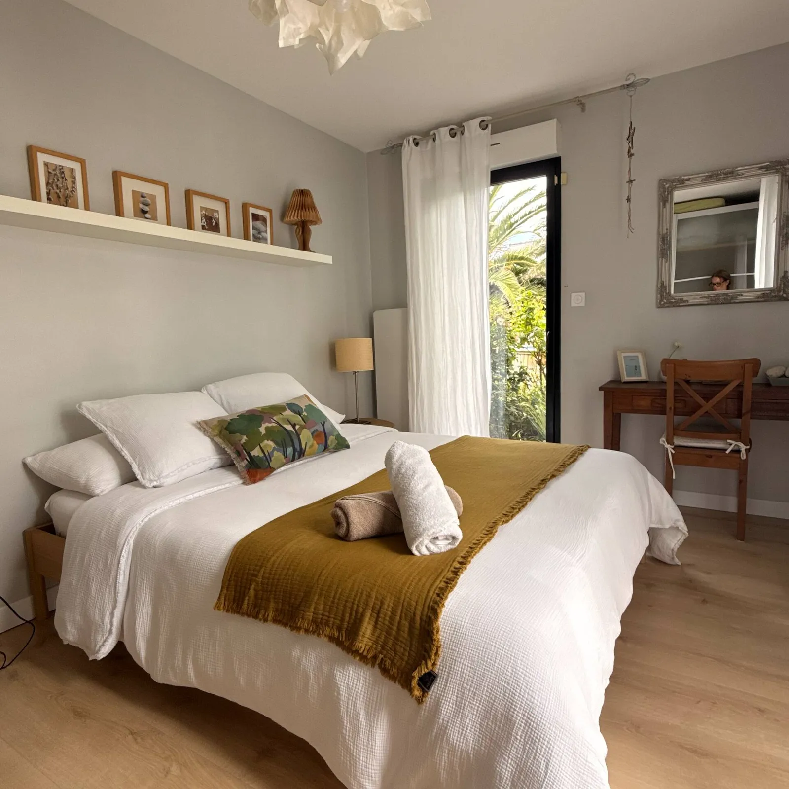 Chambre aux murs gris clair avec lit double, plaid moutarde et porte-fenêtre sur le jardin
