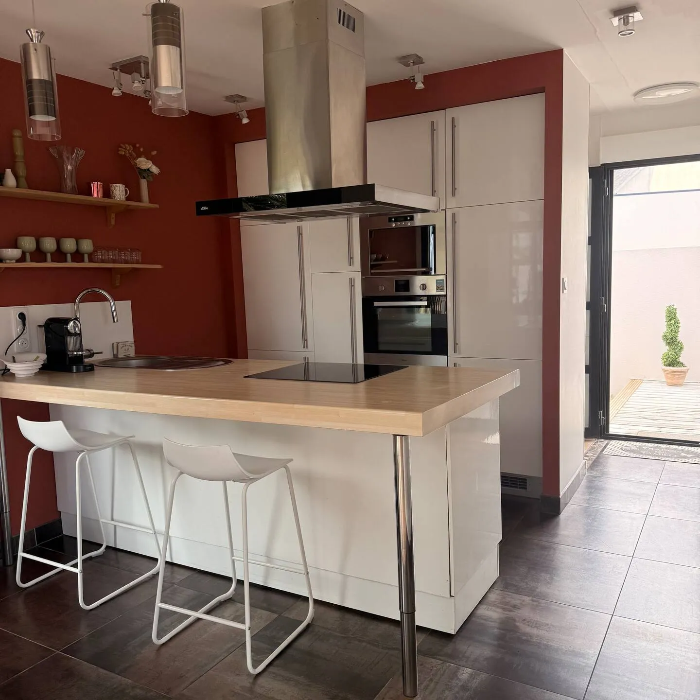 Cuisine équipée avec îlot central, plaque de cuisson, tabourets de bar et accès à la cour