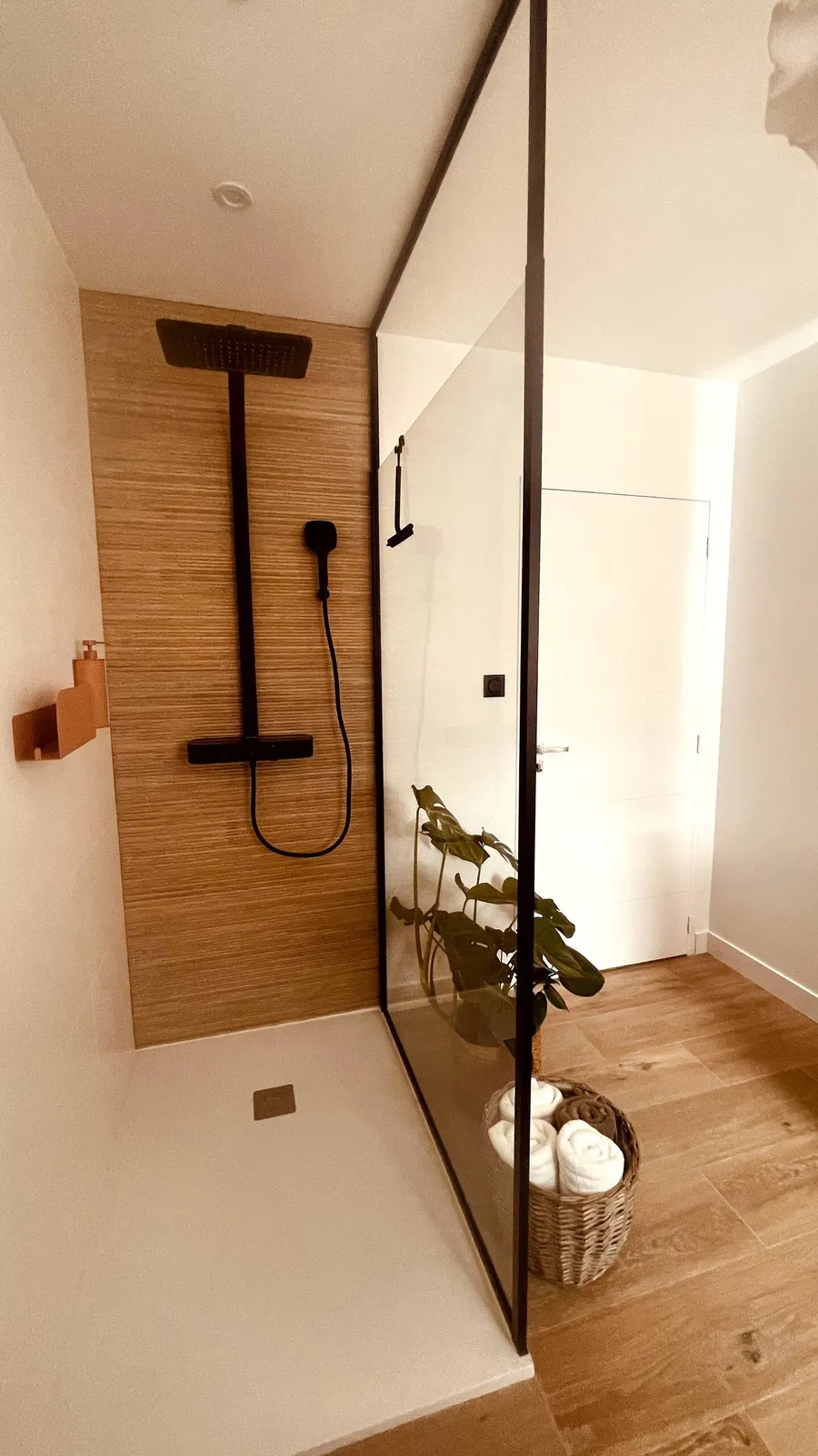 Douche à l'italienne avec paroi vitrée, colonne de douche noire et carrelage effet bois