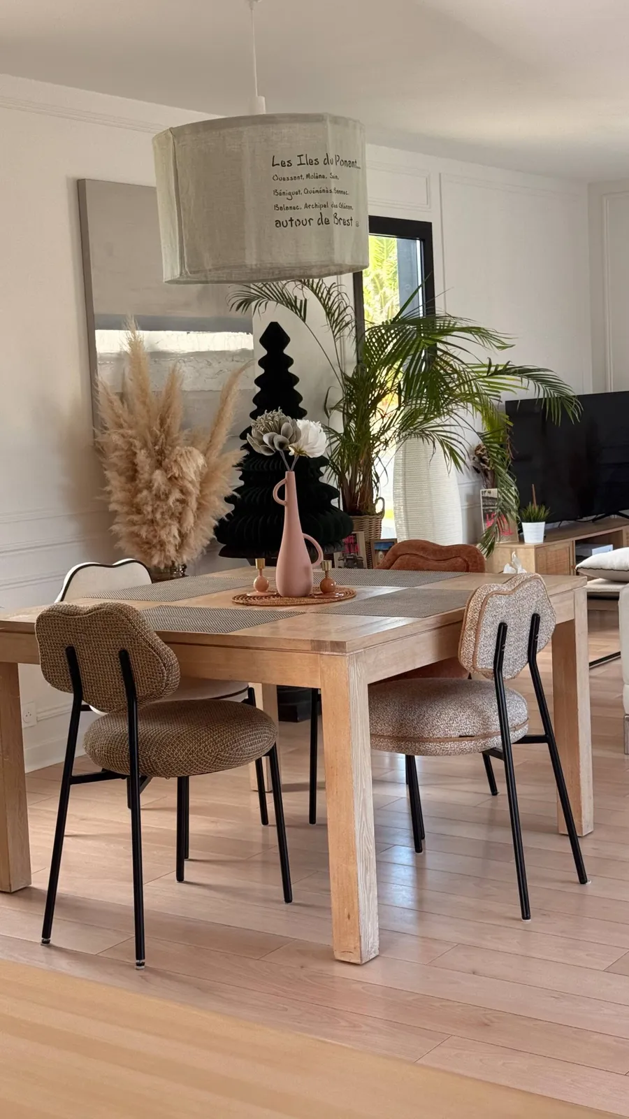 Table à manger en bois clair et chaises tapissées sous une suspension en lin, Maison Goa