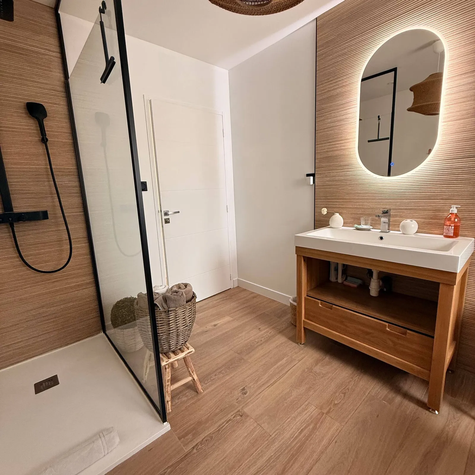 Salle de bains avec douche à l'italienne, meuble vasque en bois et miroir rétroéclairé