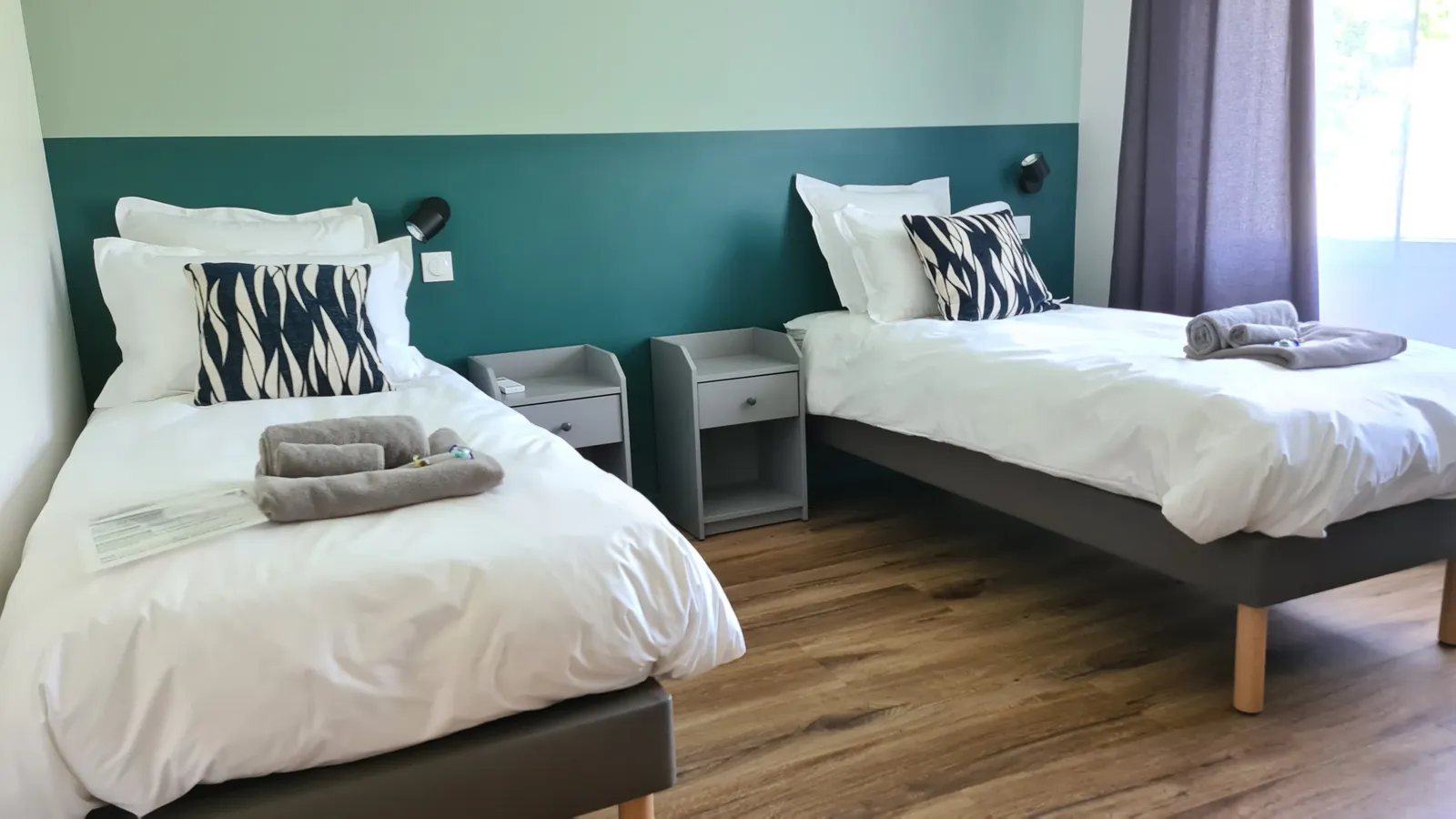 Chambre avec deux lits simples devant un mur bleu canard, gîte Sapin Zen