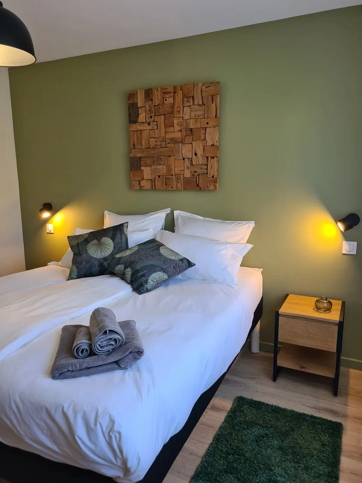 Chambre avec grand lit, tableau en bois et liseuses murales, gîte Sapin Zen