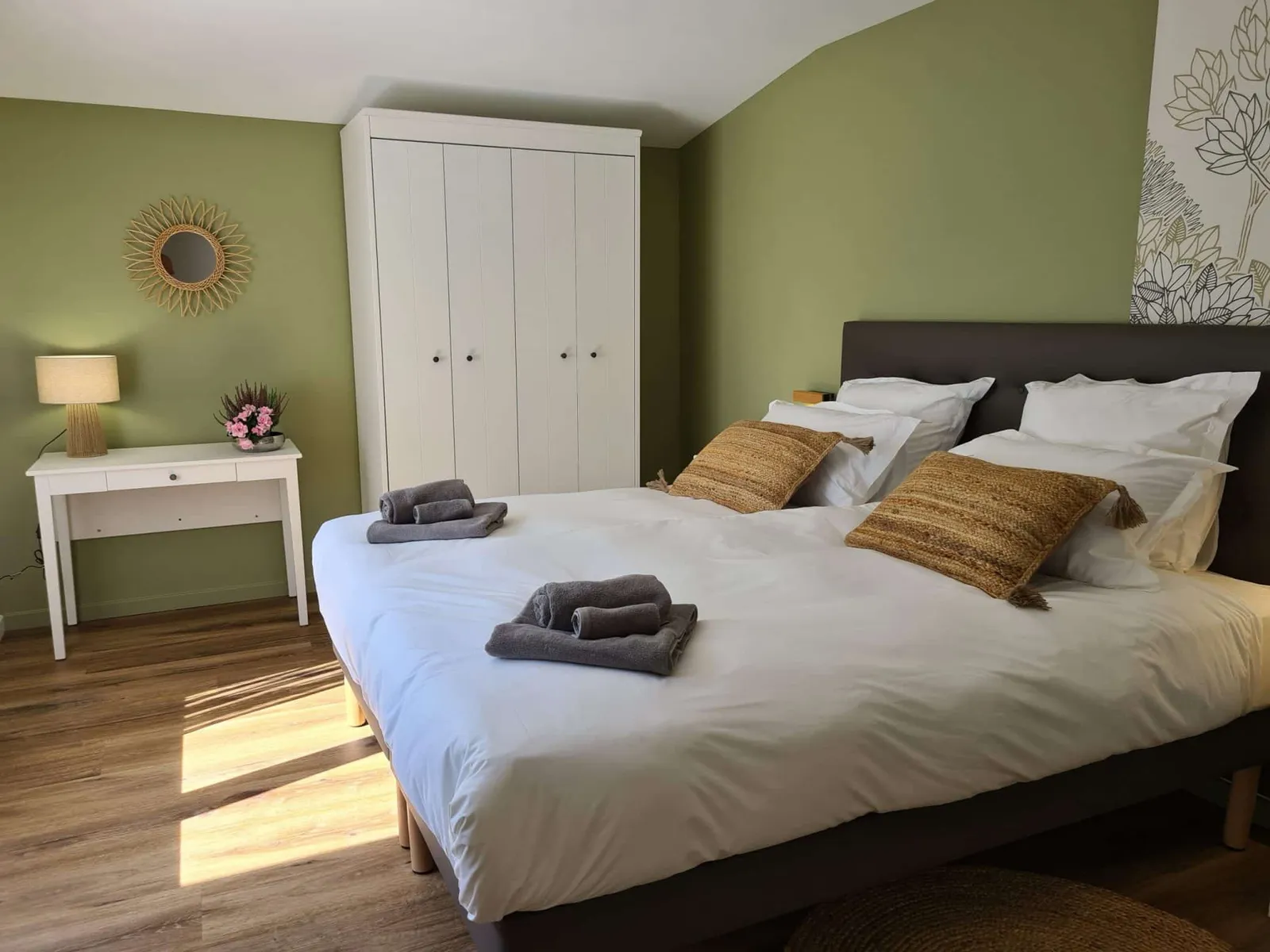 Chambre aux murs vert sauge avec grand lit, armoire blanche et miroir soleil, gîte Sapin Zen