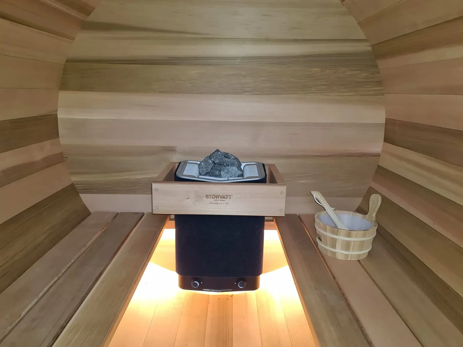 Intérieur du sauna tonneau avec poêle, bancs en bois et seau à infusion, gîte Sapin Zen