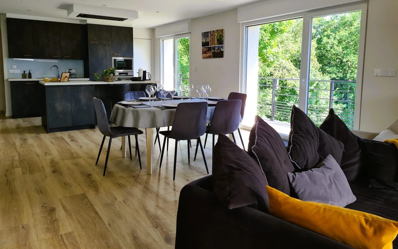 Séjour ouvert avec table dressée pour six, cuisine et baies vitrées donnant sur la forêt, gîte Sapin Zen